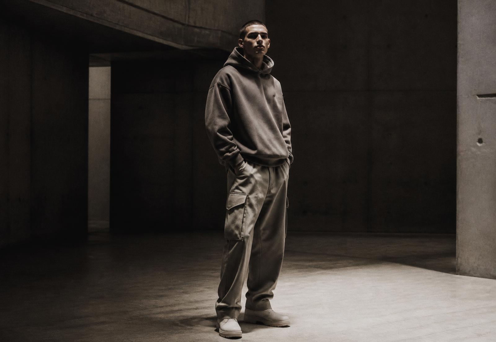 Model wearing the current NML Collection hoodie and cargo trousers in a concrete hall